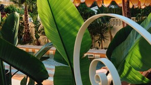 A poolside area with lounge chairs, a large umbrella, and tropical plants. - Riviera Hotel Menorca  (Ciutadella de Menorca)