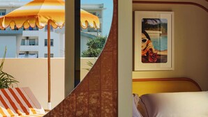 A hotel room with a bathroom, a bed, a large mirror, and a view of buildings and an umbrella outside. - Riviera Hotel Menorca  (Ciutadella de Menorca)