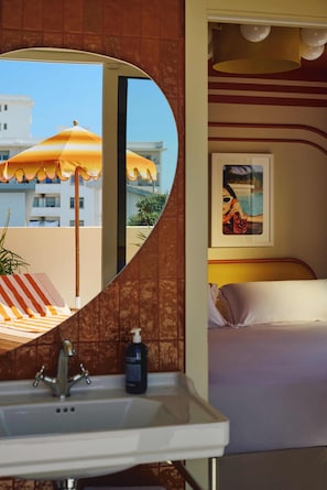 Une chambre d’hôtel avec salle de bain, un lit, un grand miroir et une vue sur les bâtiments, ainsi qu’un parapluie à l’extérieur.