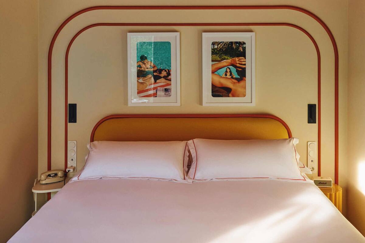 A bed with a wooden headboard, a bedside table with a telephone, and a wall-mounted light fixture.