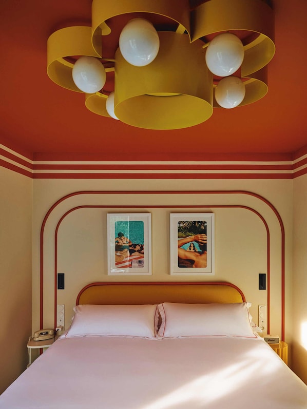 A bed with a wooden headboard, a bedside table with a telephone, and a wall-mounted light fixture. - Riviera Hotel Menorca (Ciutadella de Menorca)