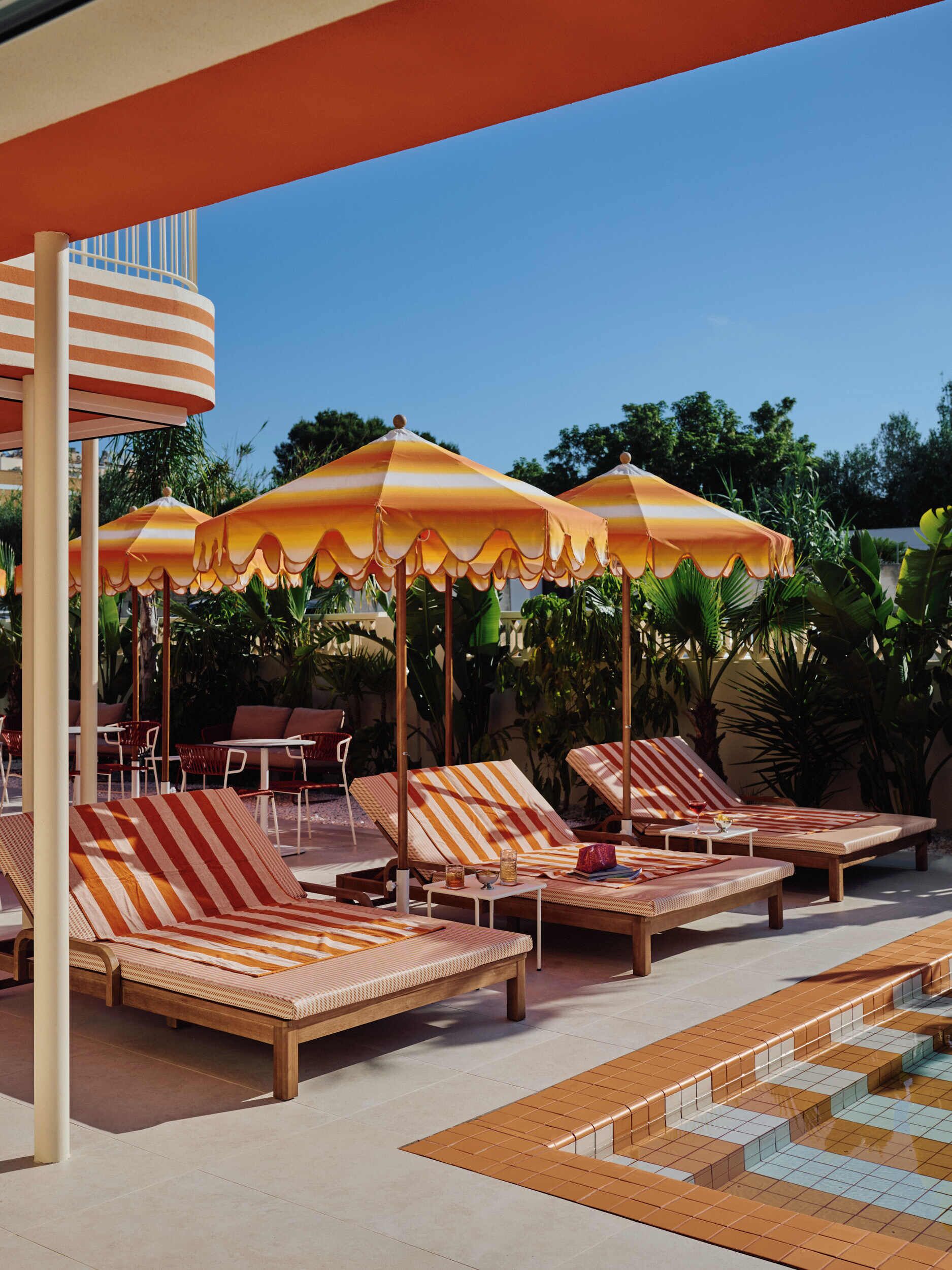 Un espace aménagé au bord de la piscine, avec des chaises longues à rayures, des parasols orange et blancs à rayures, et une piscine carrelée.