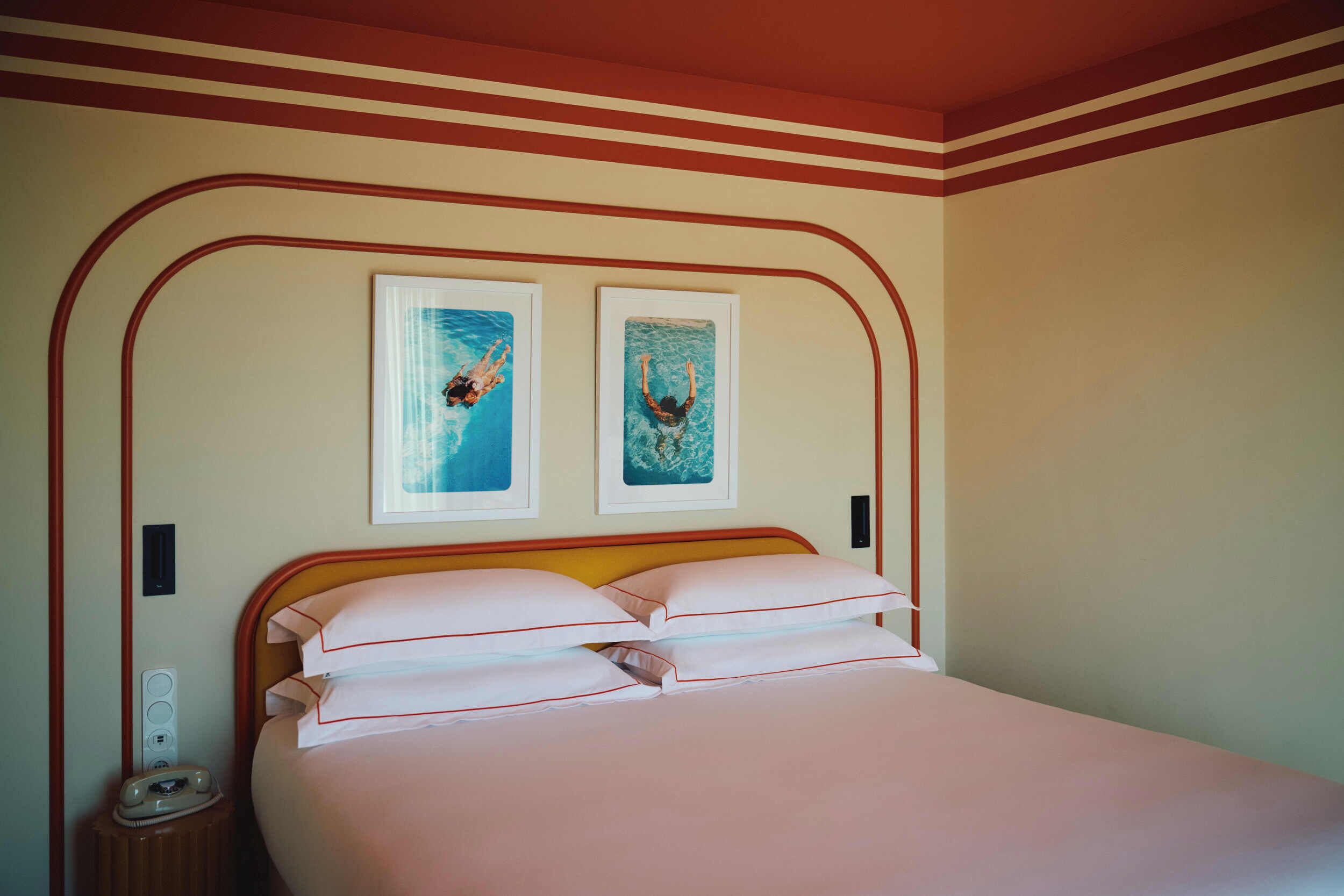 A hotel room with a bed, two framed pictures on the wall, a bedside table, and a nightstand.