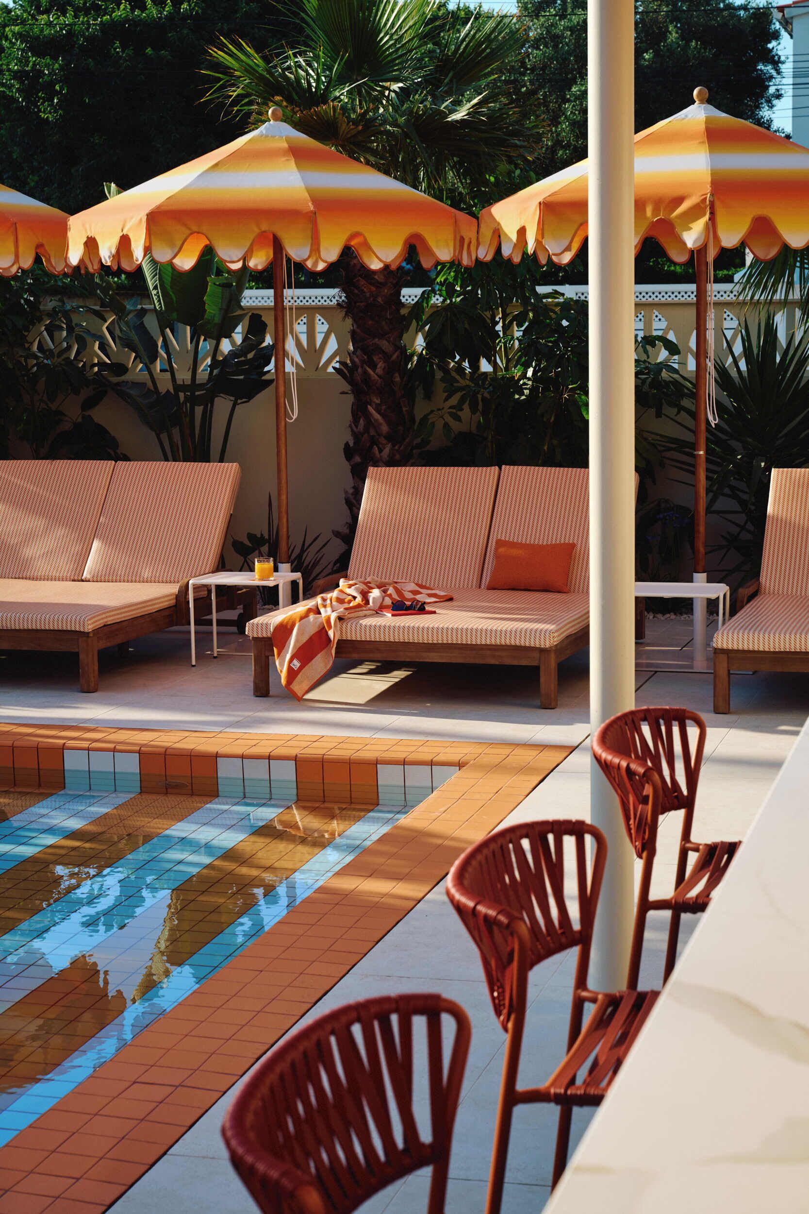 A poolside area with lounge chairs, umbrellas, and a tiled pool.