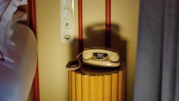 Une chambre d’hôtel avec un lit, un téléphone sur une petite table, une prise électrique et un interrupteur fixé au mur.