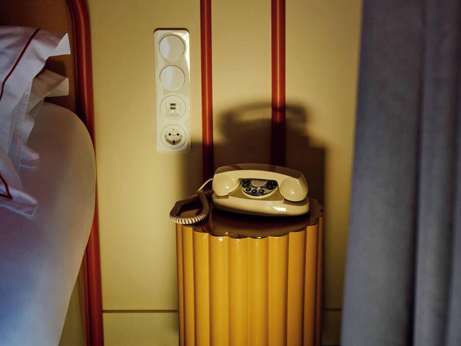 Une chambre d’hôtel avec un lit, un téléphone sur une petite table, une prise électrique et un interrupteur fixé au mur.
