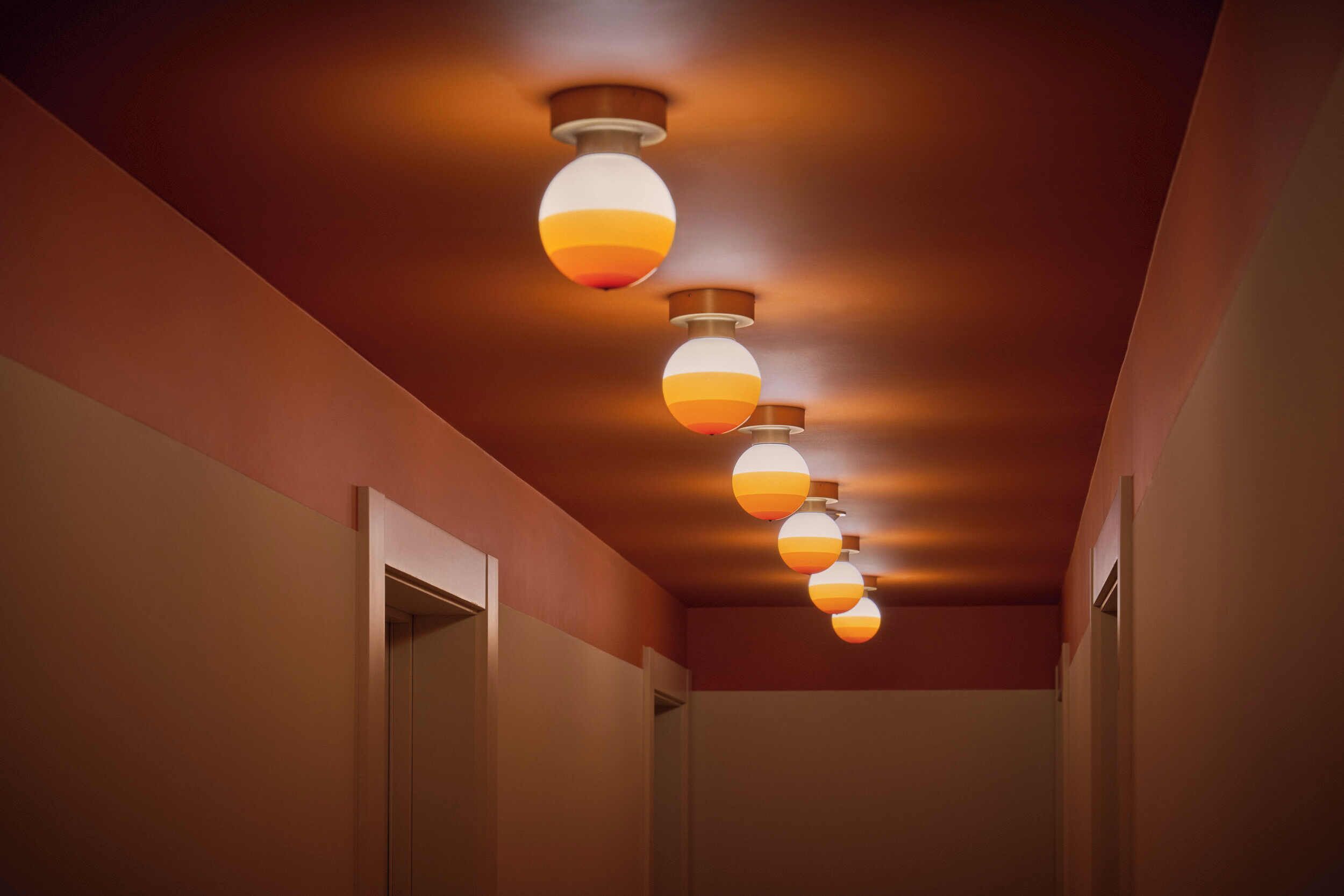 A hallway with a series of spherical pendant lights and a door on the left.