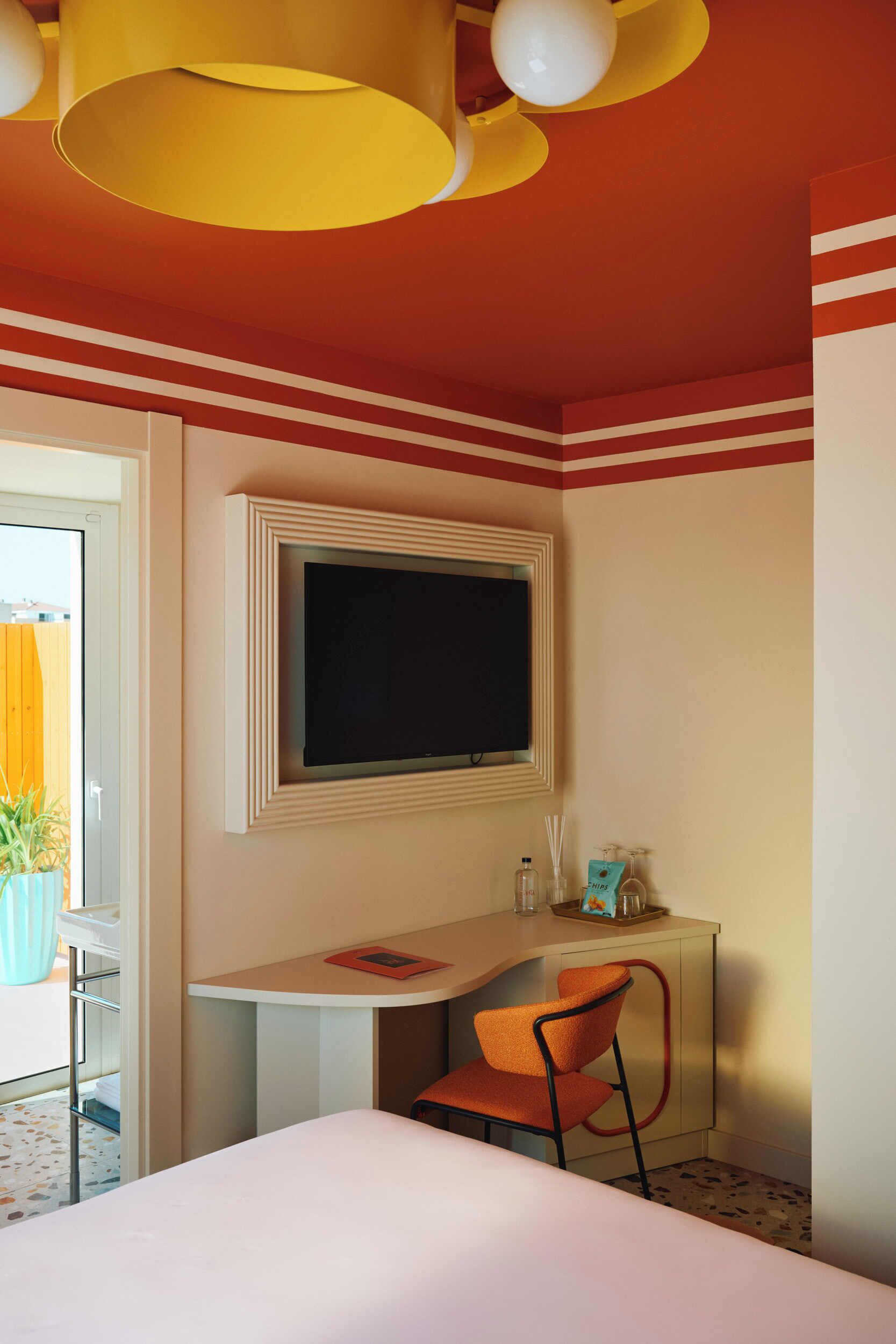 A hotel room with a bed, a desk with a chair, a television mounted on the wall, and a window.
