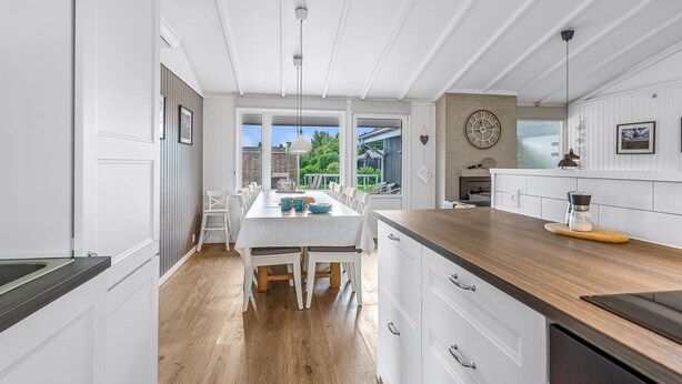 A modern kitchen with white cabinetry, a wooden countertop, and a dining area with a table and chairs.
