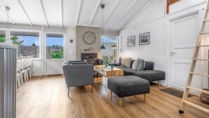 A spacious living area with a sofa, ottoman, and chairs, a wooden floor, and a large window offering a view of the outdoors.