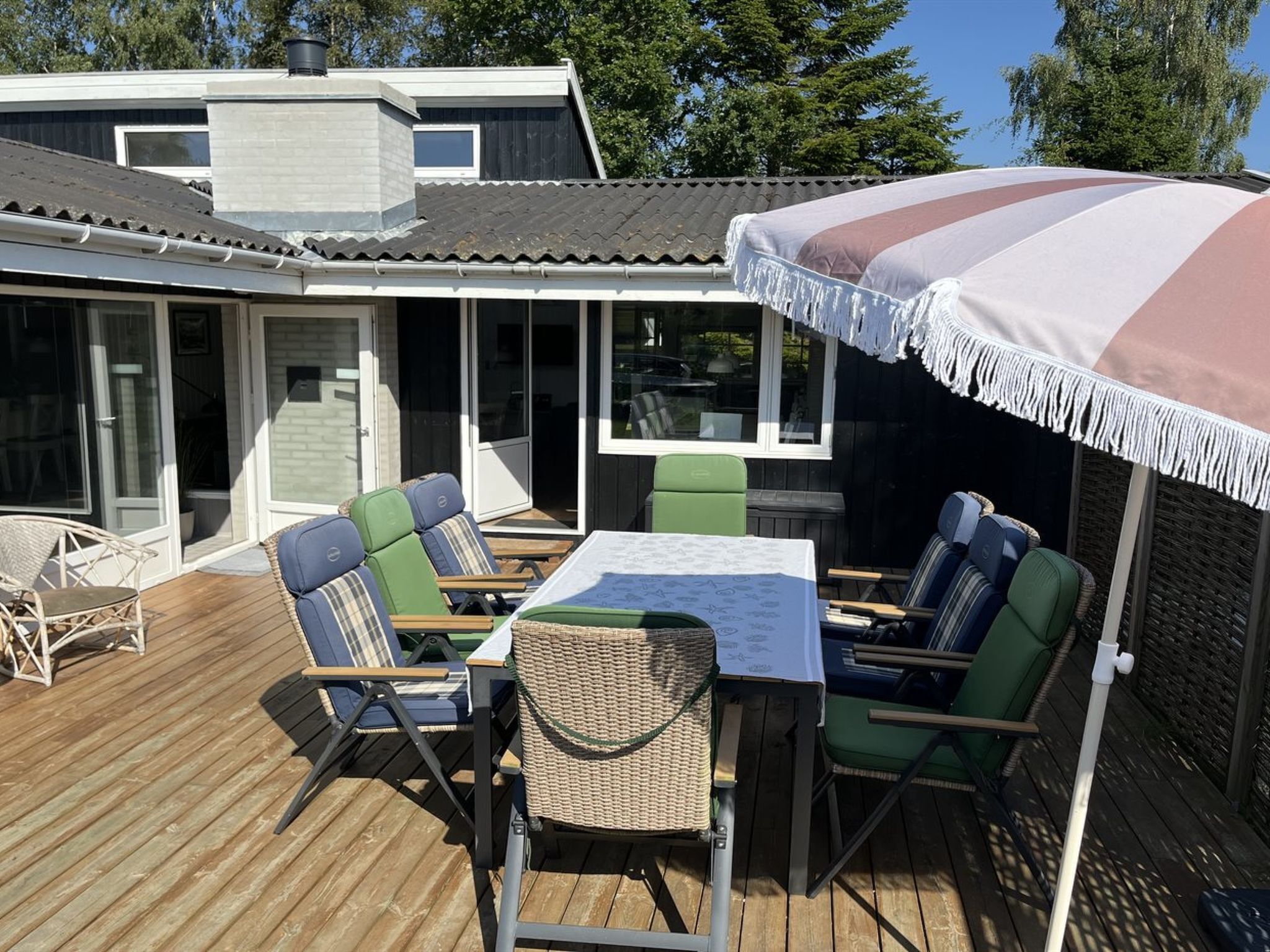 An outdoor patio with a table and chairs, a covered area with a striped canopy, and a house in the background.