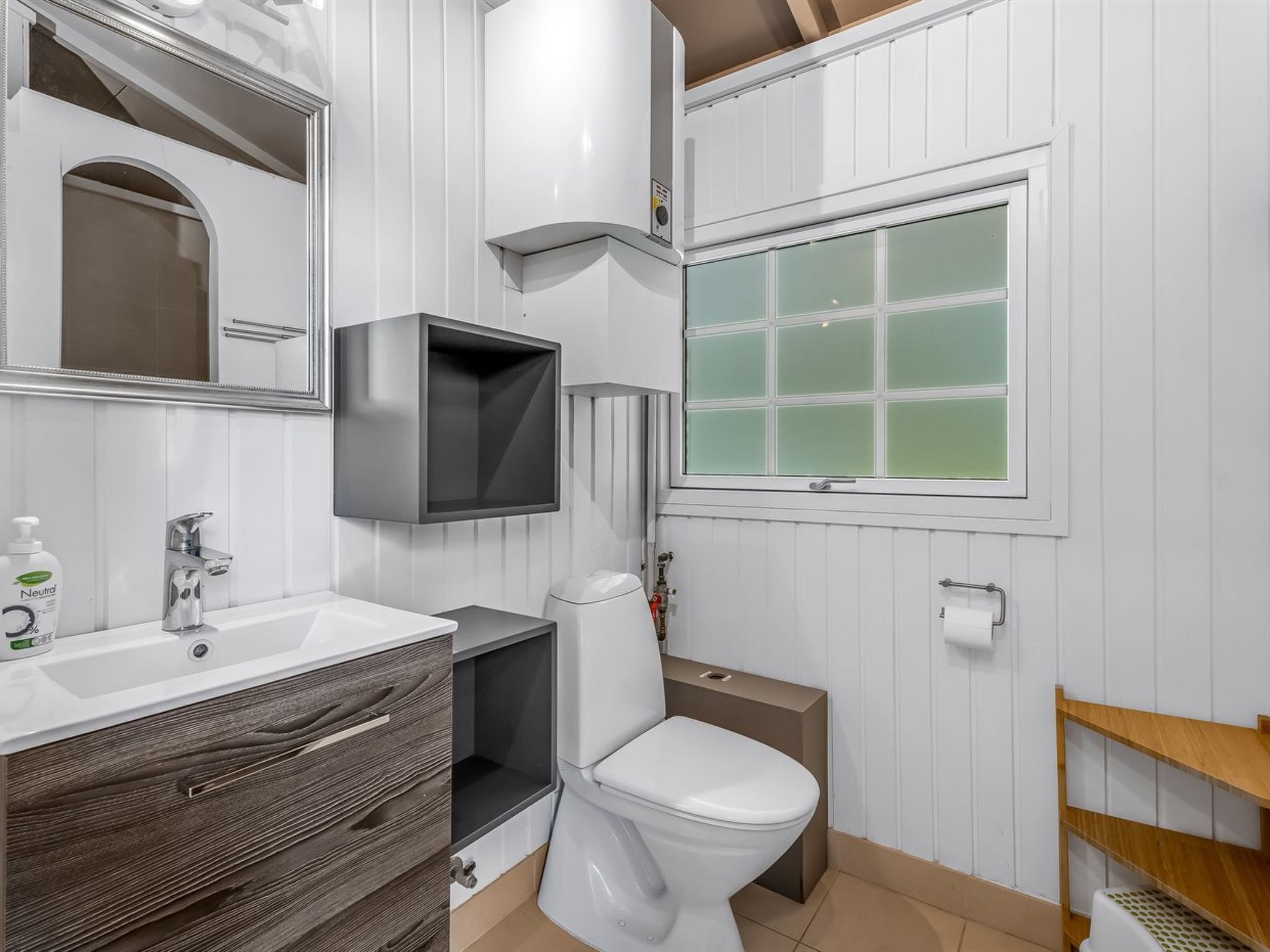 A modern bathroom with a white vanity, a toilet, a window with frosted glass, and a mirror above the sink.