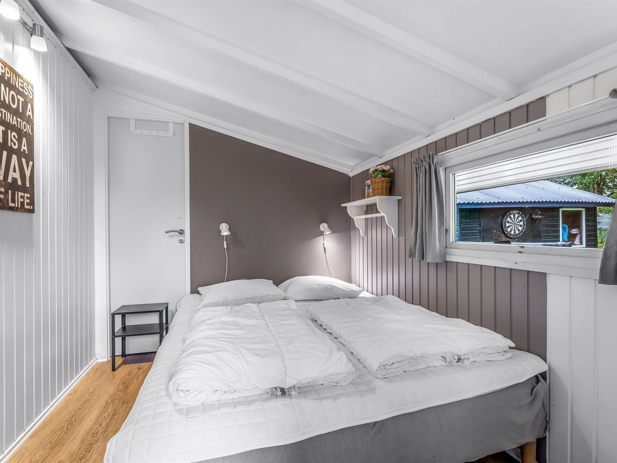 A bedroom with a bed, bedside tables, a window with a view, and a wall-mounted shelf with a basket.