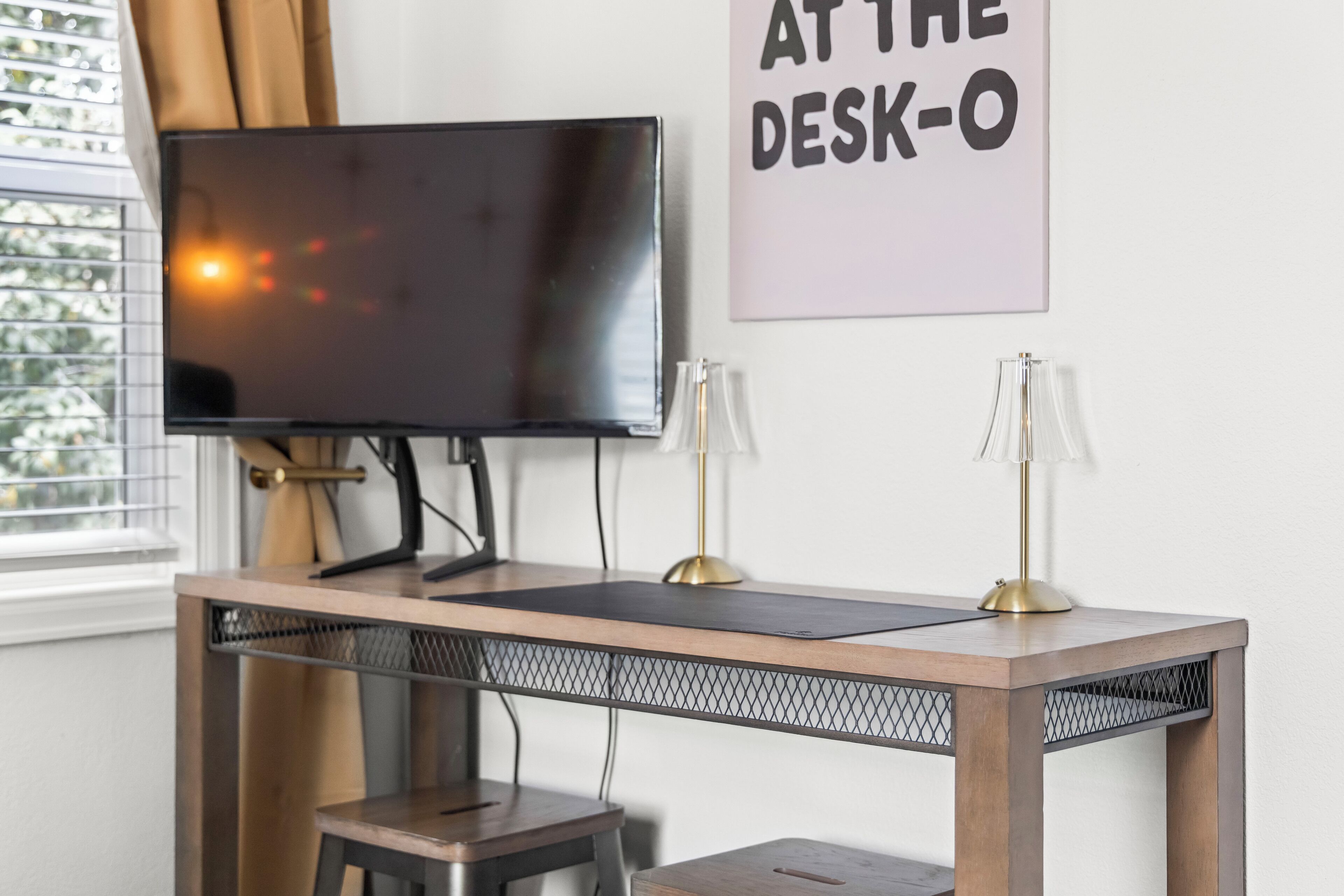 A desk with a television, two lamps, and a sign that reads 'AT THE DESK-O'.