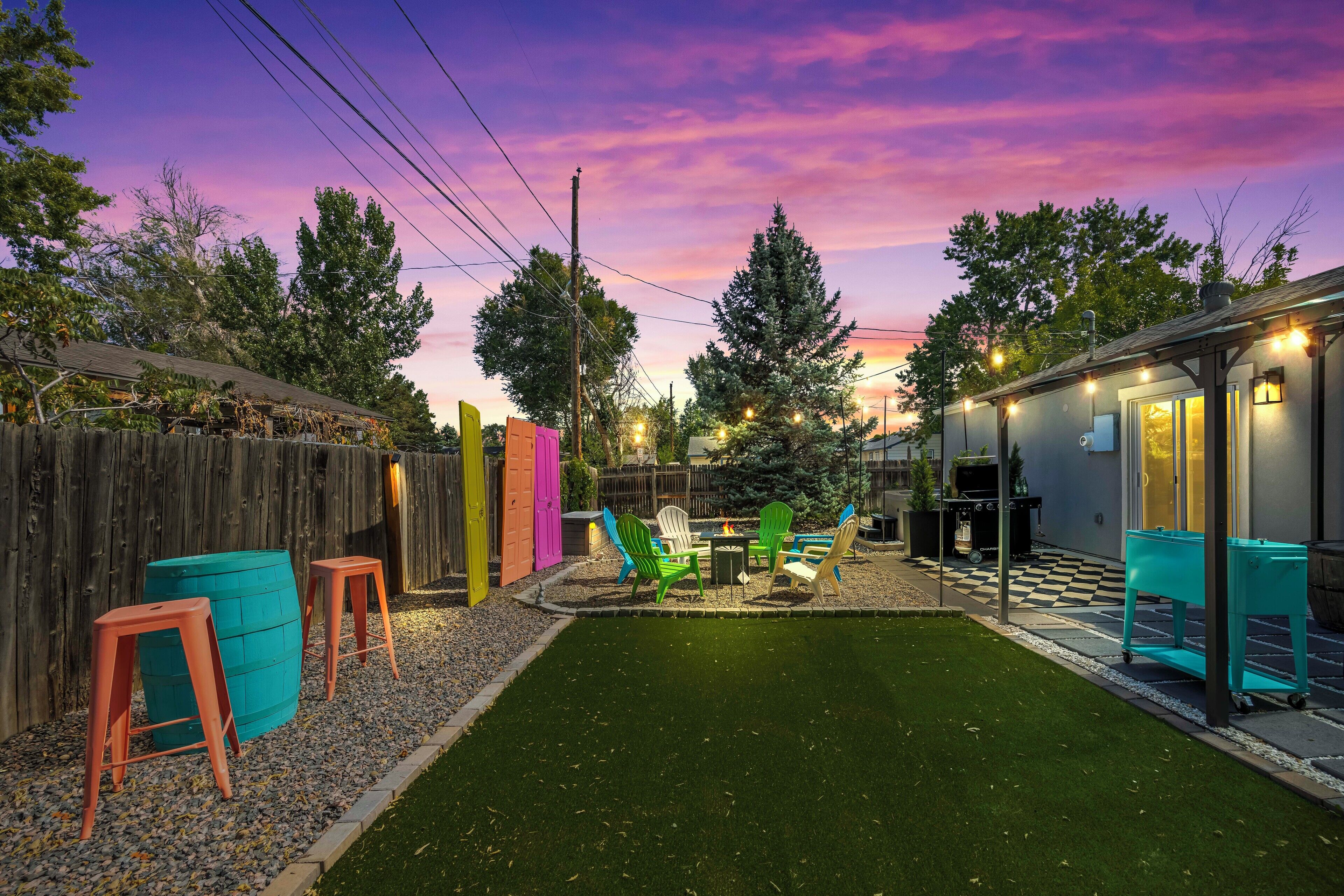 A backyard with artificial grass, a fire pit, and colorful Adirondack chairs.
