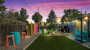 A backyard with artificial grass, a fire pit, and colorful Adirondack chairs.