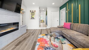 A modern living room with a fireplace, a sectional sofa, and a colorful rug. - Olde Town Gem: 5 TVs + Hot Tub & Game Yard (Arvada)