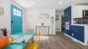 A bright kitchen with white cabinets, a blue accent wall, and a rainbow-patterned tablecloth. - Olde Town Gem: 5 TVs + Hot Tub & Game Yard (Arvada)