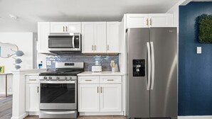A modern kitchen with white cabinets, stainless steel appliances, and a blue accent wall. - Olde Town Gem: 5 TVs + Hot Tub & Game Yard (Arvada)