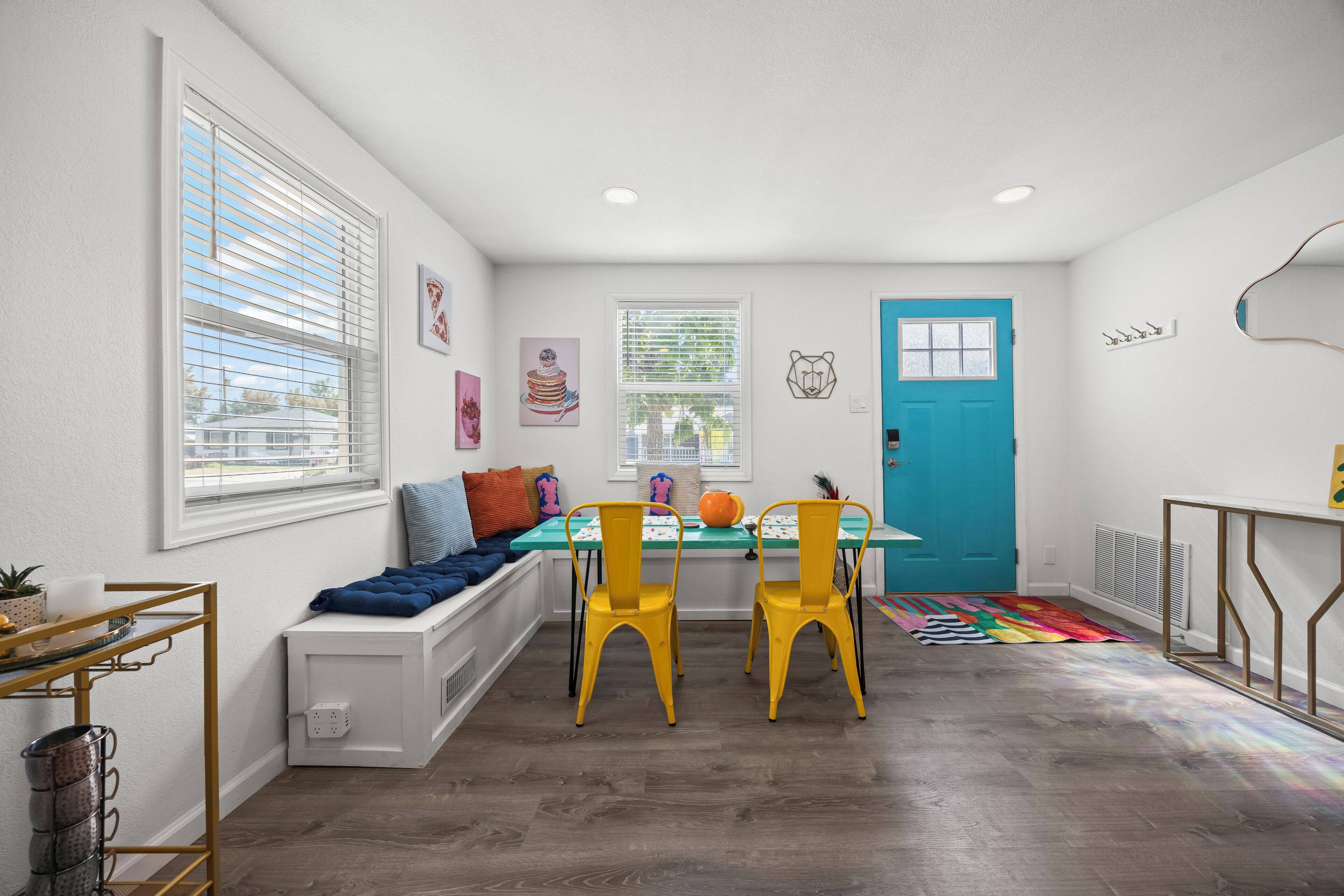 A room with a white bench, two yellow chairs, a blue door, and a colorful rug.