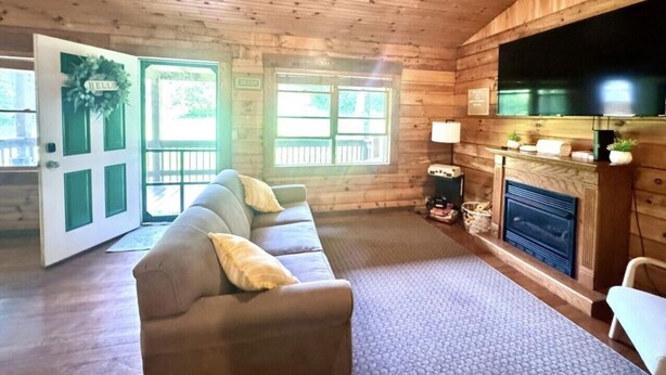 A log cabin interior with a sofa, fireplace, and a door leading outside. - Delightful cabin with Fireplace in charming Canvas (Canvas)