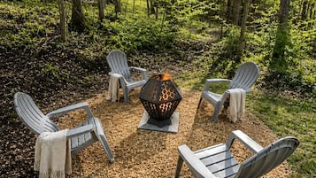 Un aménagement circulaire avec des sièges, composé de quatre fauteuils Adirondack disposés autour d’un foyer central, le tout situé dans un cadre forestier.