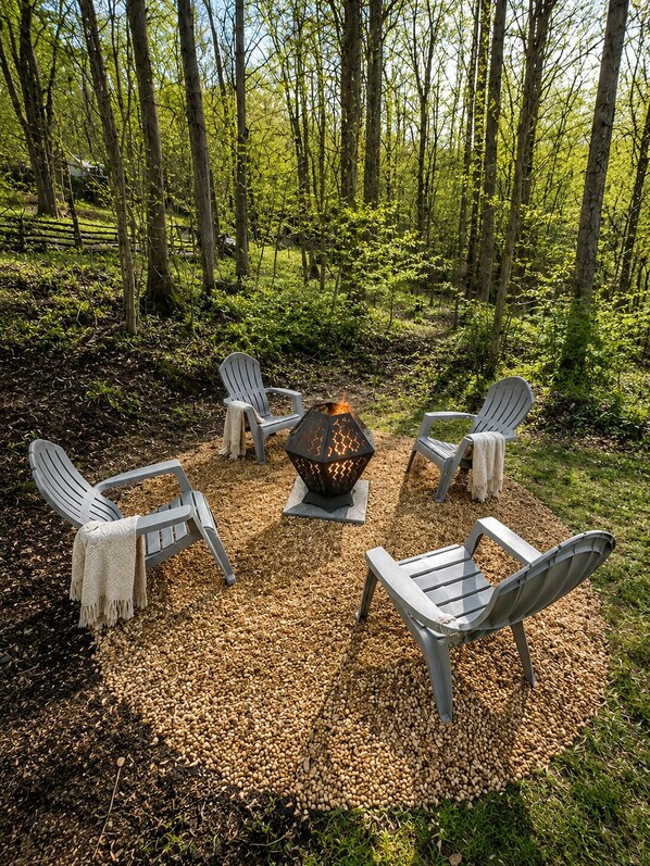 A circular seating arrangement with four Adirondack chairs around a central fire pit in a forest setting. - Delightful cabin with Fireplace in charming Canvas (Canvas)