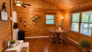 Interior de madera con una mesa de comedor, sillas, un ventilador de techo y una ventana con persianas.