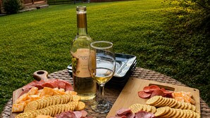 Un montaje para picnic al aire libre con una variedad de quesos, embutidos, galletas y una botella de vino sobre una mesa de mimbre.