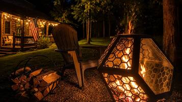Una terraza de madera con una fogata hexagonal, una silla y leña apilada.
