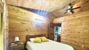 A wooden-paneled bedroom with a bed, nightstand, lamp, and ceiling fan. - Delightful cabin with Fireplace in charming Canvas (Canvas)