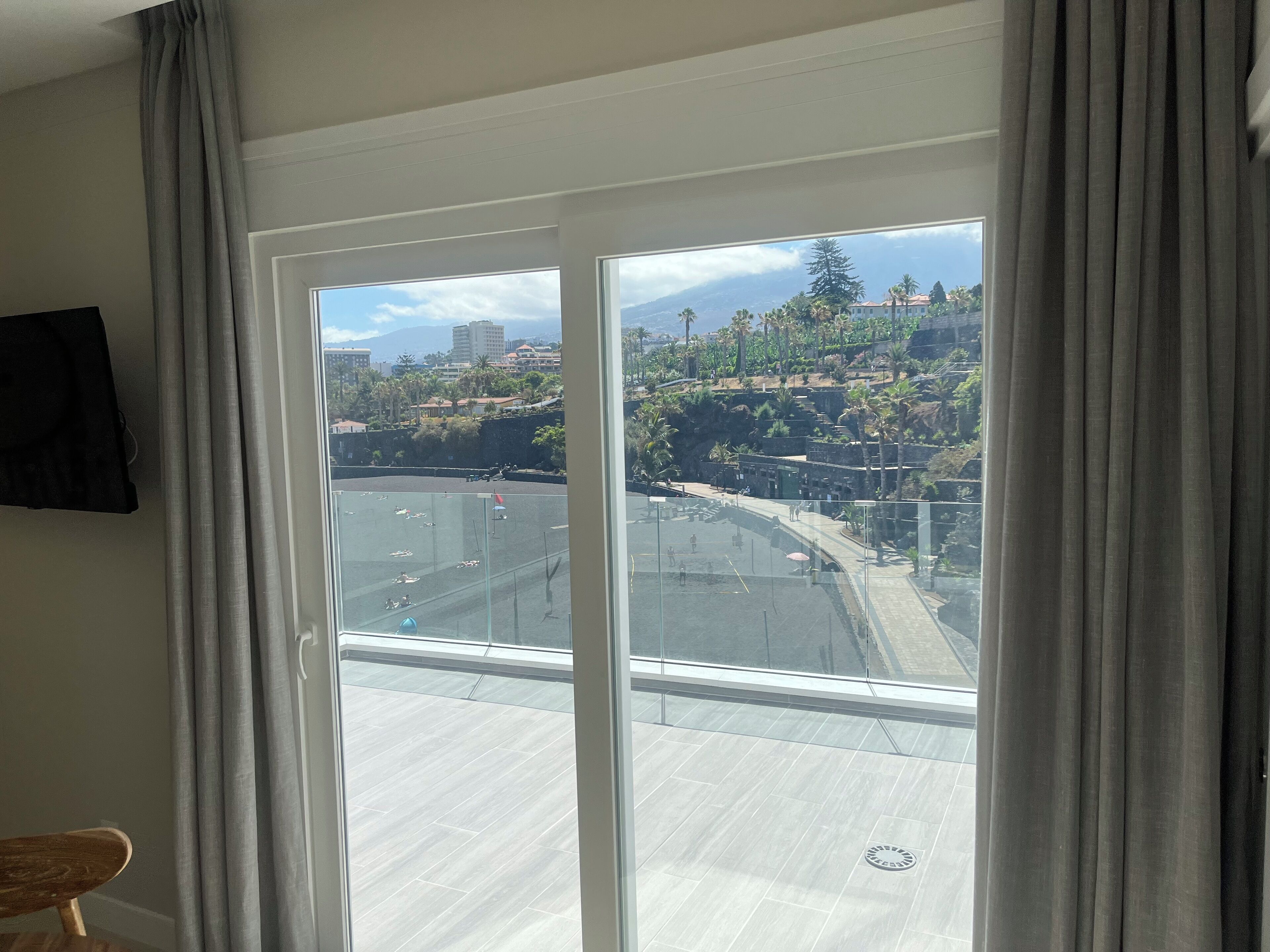 Una habitación con un amplio ventanal corredera que da a un balcón con vistas a un paisaje urbano y colinas.