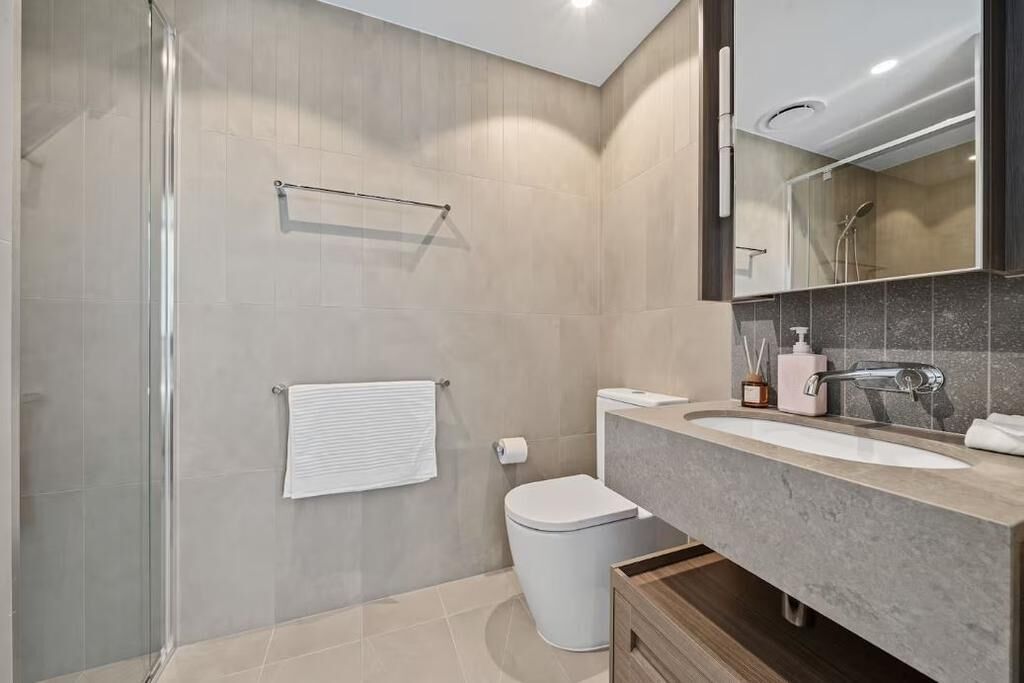 Un baño moderno con cabina de ducha de vidrio, inodoro, lavabo con encimera de mármol y espejo sobre el lavabo.
