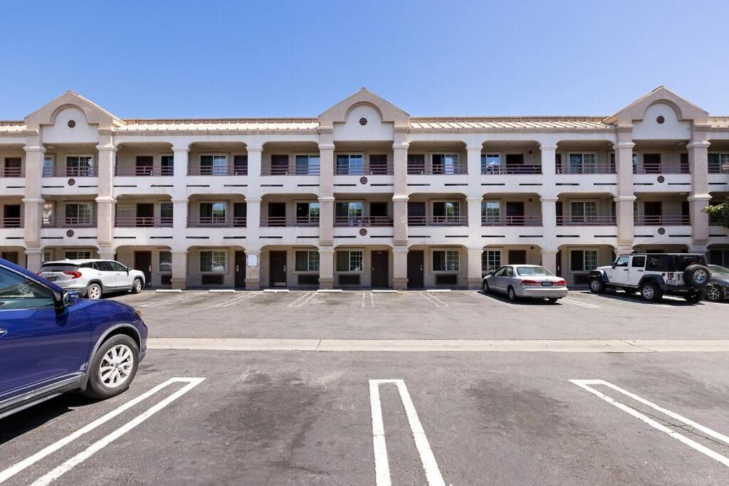 A multi-story hotel with a symmetrical facade, multiple balconies, and a parking lot with several cars.