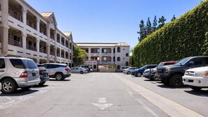 Un parking où sont garées plusieurs voitures, devant un bâtiment de style architectural classique, caractérisé par des colonnes et une cour intérieure.