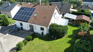 Una casa con paneles solares en el techo, un césped cuidado y una pequeña zona ajardinada.