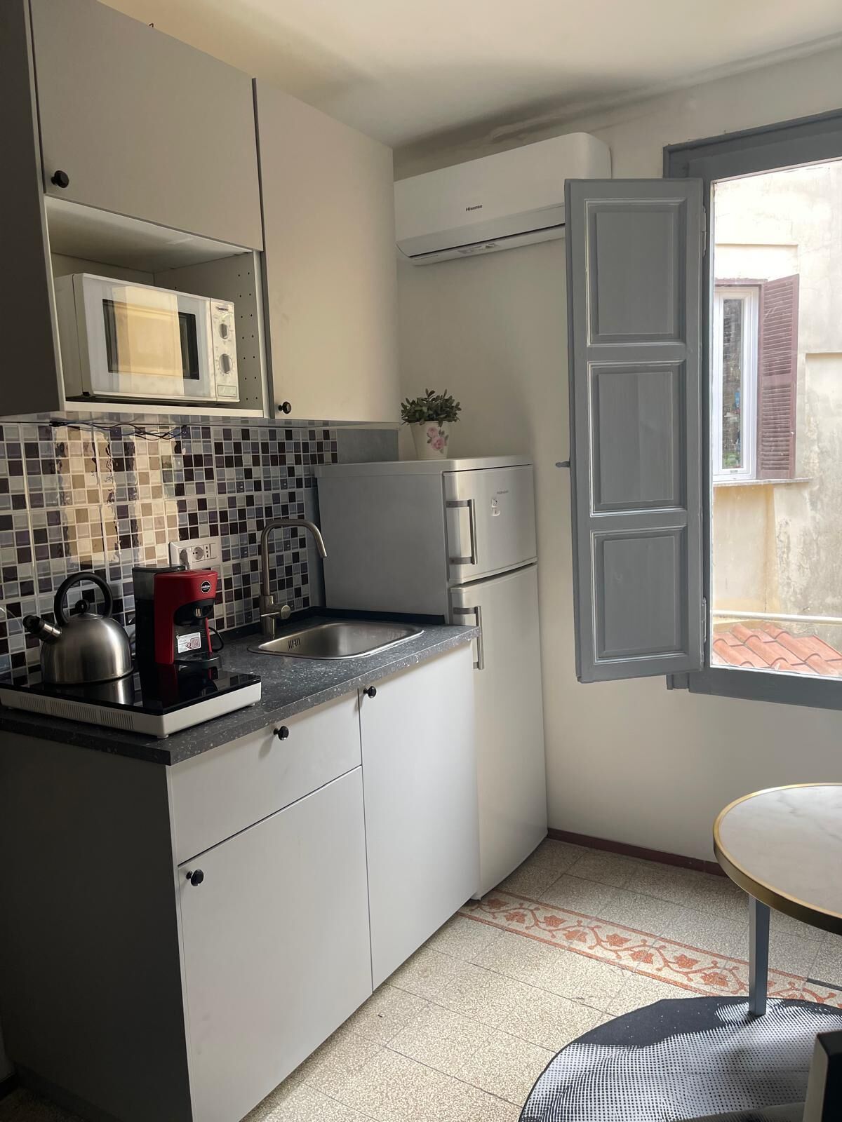 Uma cozinha compacta com armários brancos, micro-ondas, cafeteira e chaleira no balcão.