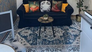 Un salon avec un canapé noir, un tapis à motifs et un tableau représentant un pont.