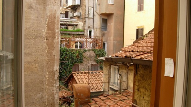 Une ruelle étroite, bordée d’immeubles aux toits couverts de tuiles et agrémentée de quelques plantes.