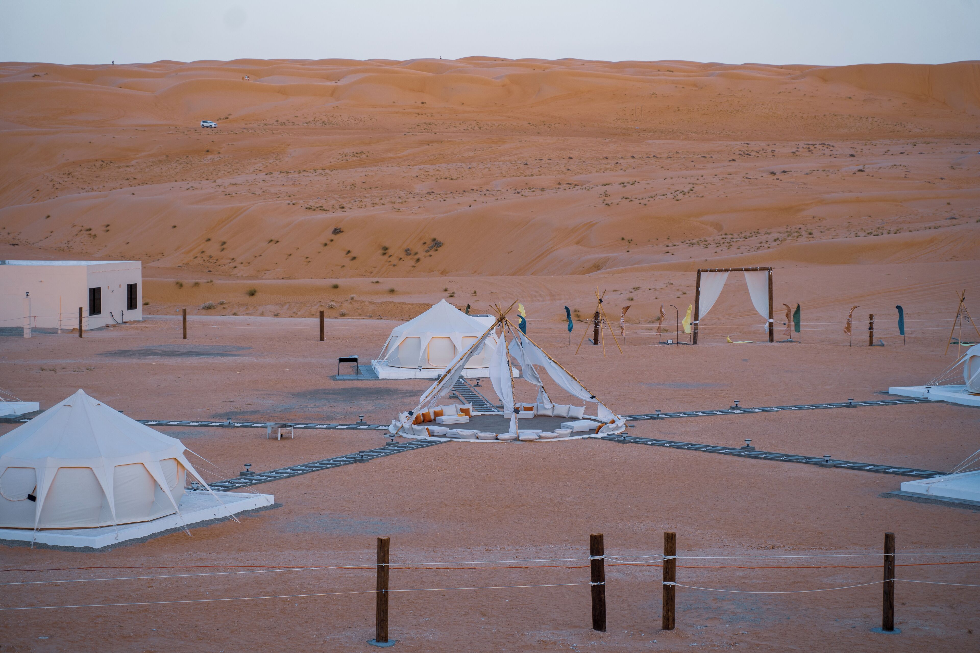 Un campamento en el desierto con tiendas de campaña y una estructura central, rodeado de dunas de arena.