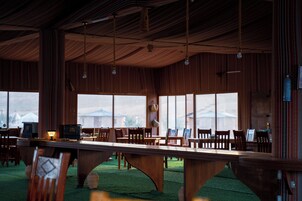 Una habitación amplia con una larga mesa de madera, varias sillas y grandes ventanales que ofrecen vistas al exterior.