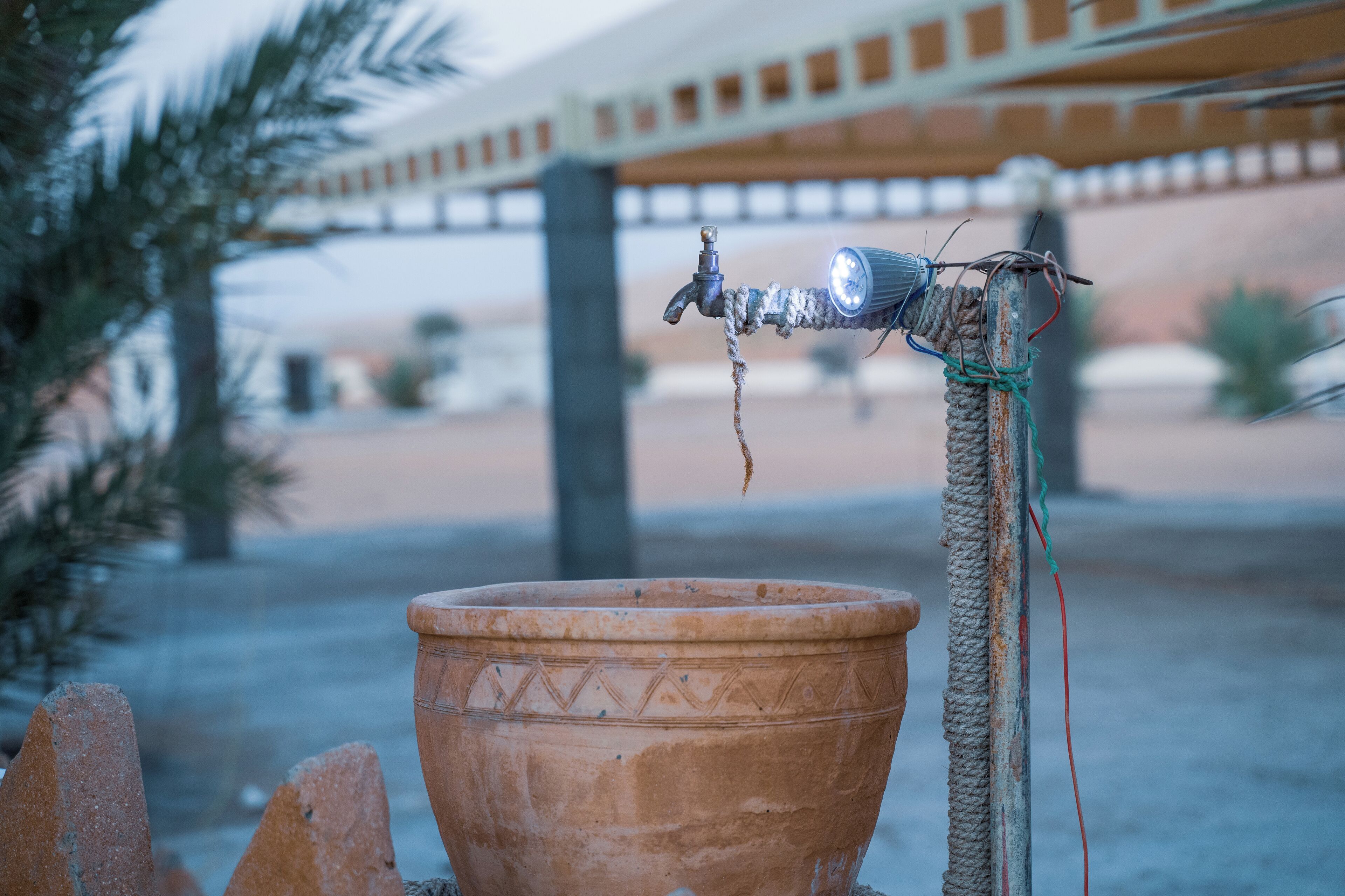 A terracotta pot with a rope and a metal object attached to a post.