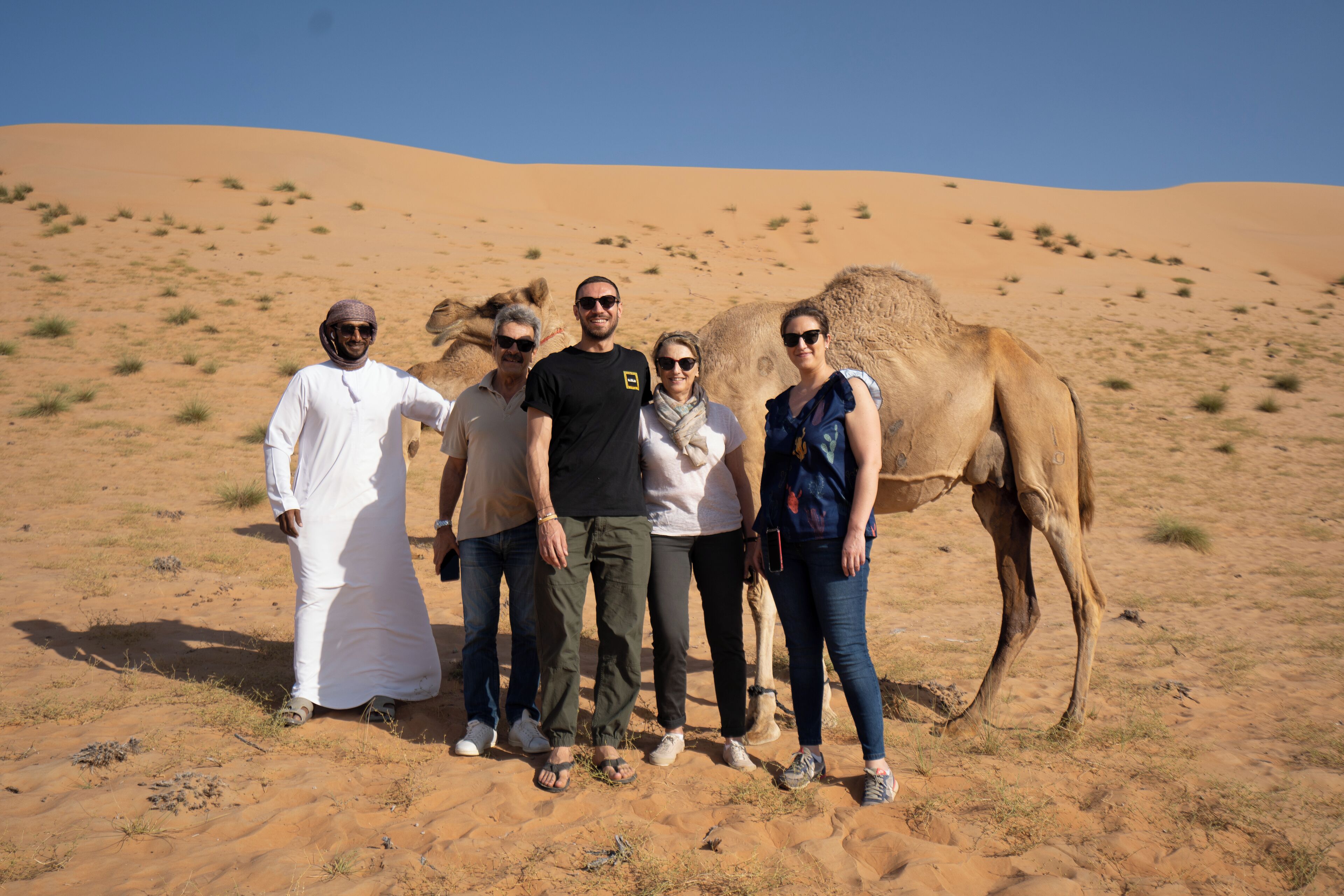 A group of people standing in a desert with sand dunes in the background.