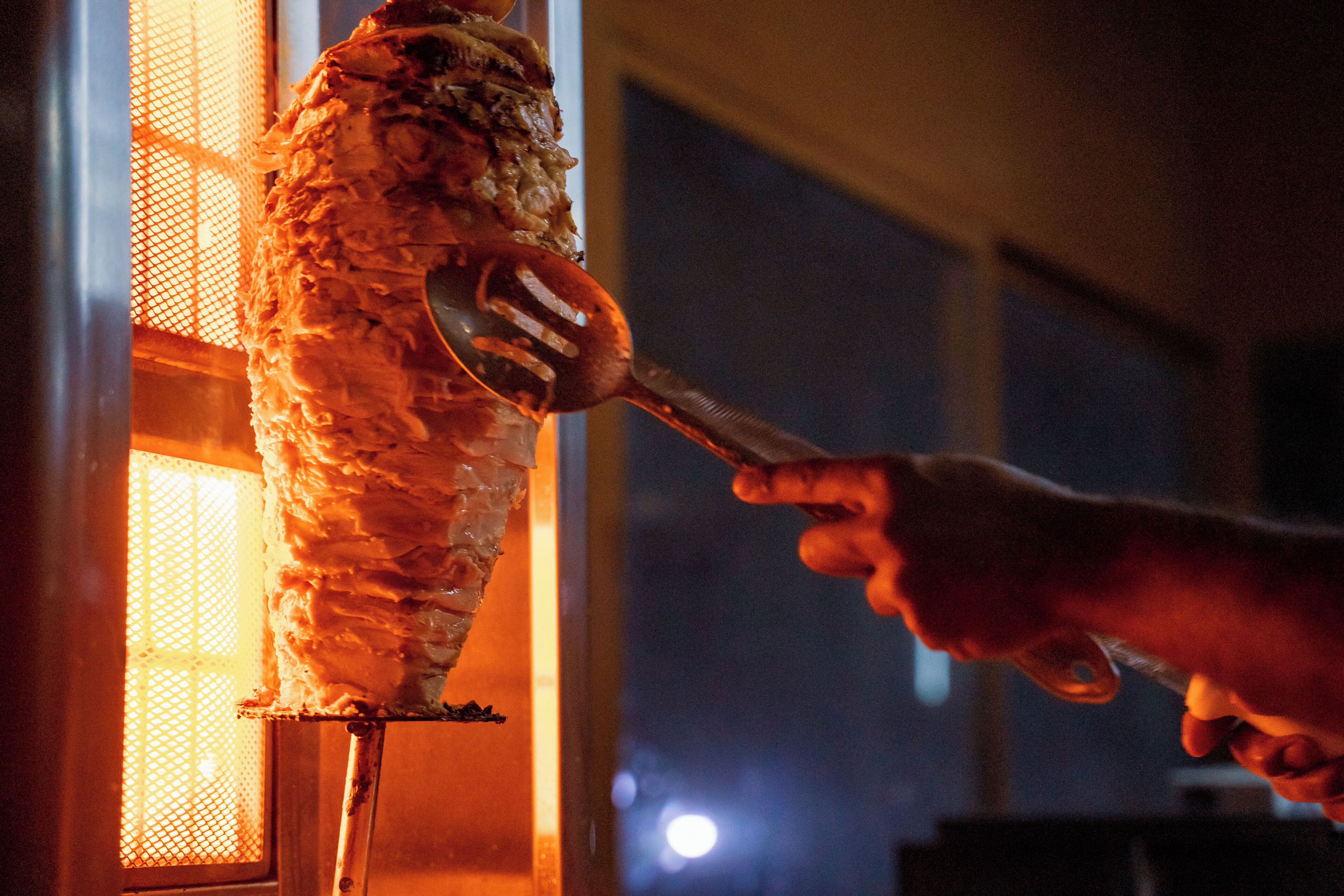 A hand using a spatula to serve food from a vertical rotisserie.