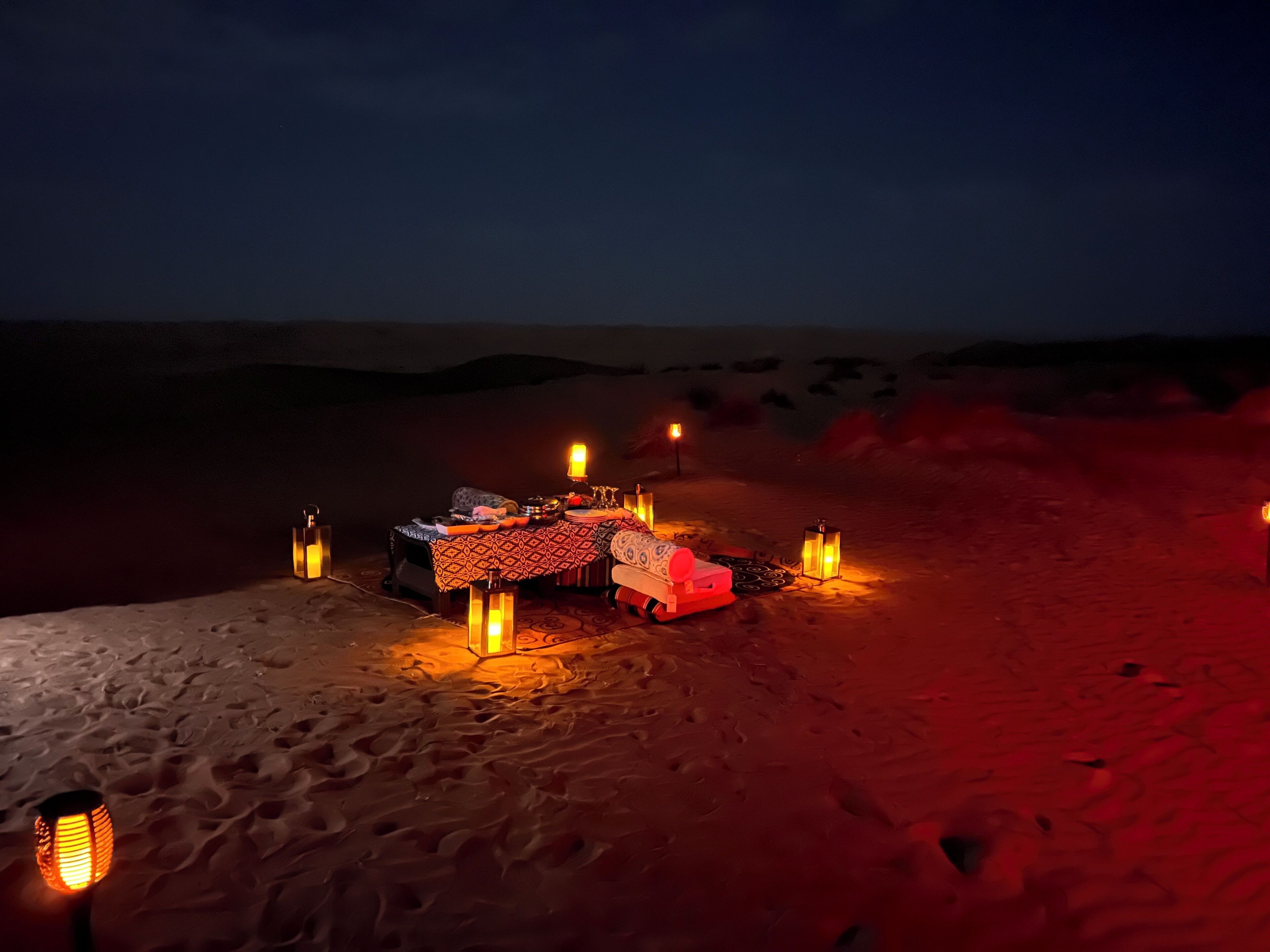 A desert campsite with a table set up for dining, surrounded by lanterns.