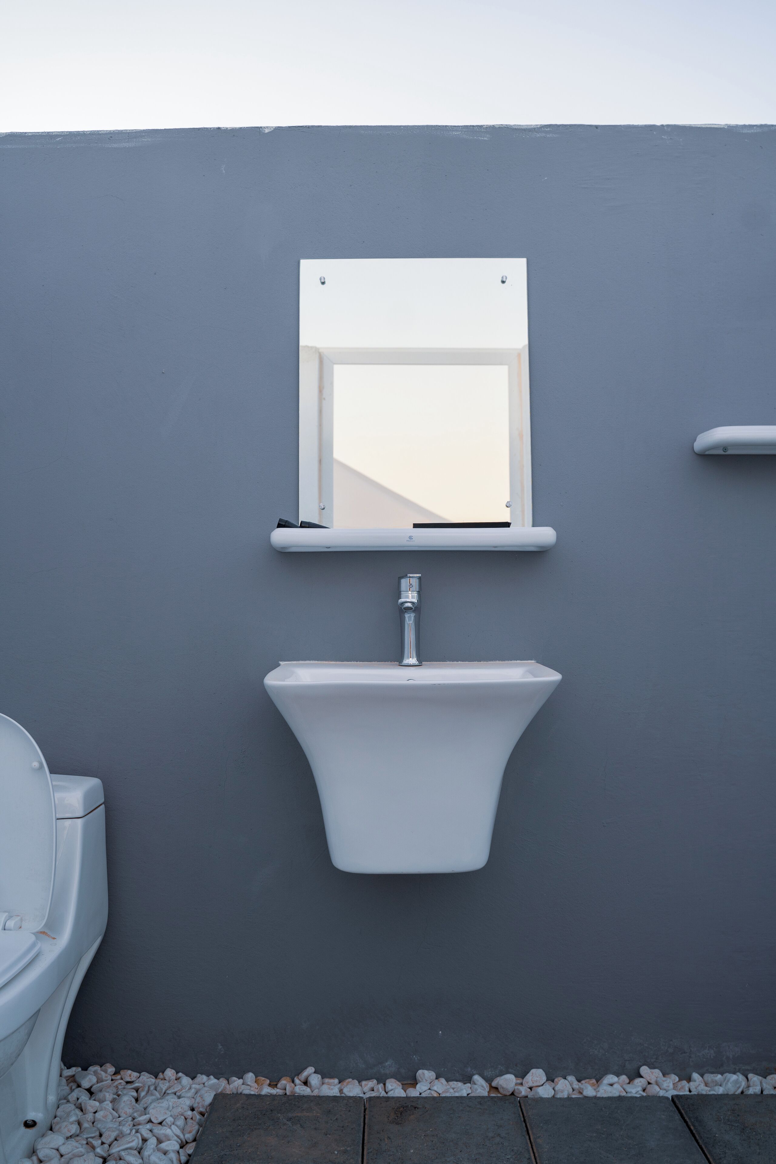 A bathroom with a white sink, a mirror, and a toilet against a grey wall.