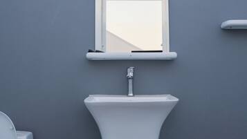 A bathroom with a white sink, a mirror, and a toilet against a grey wall.