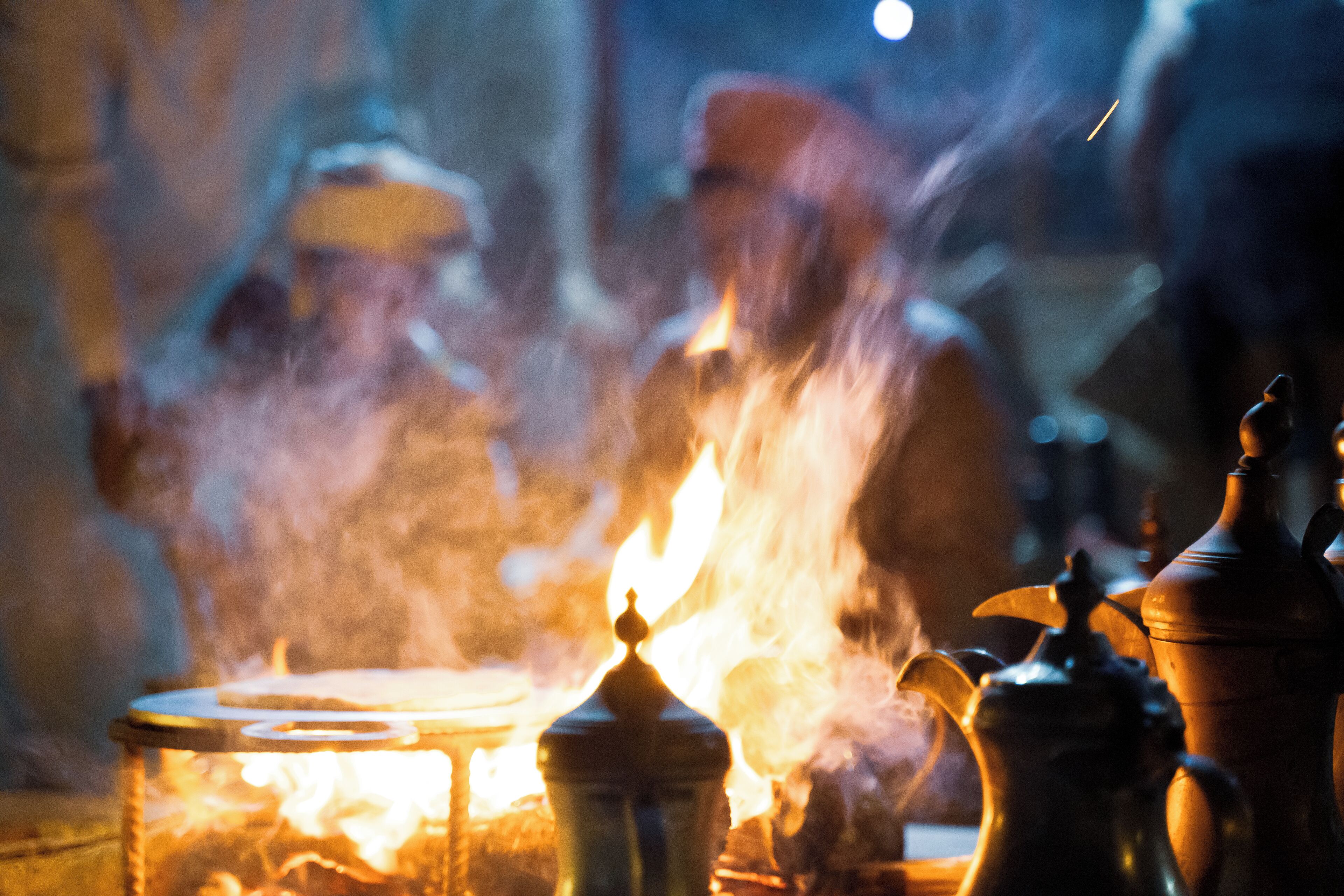 A close-up of a traditional tea set with a teapot and cups, surrounded by smoke from a nearby fire.