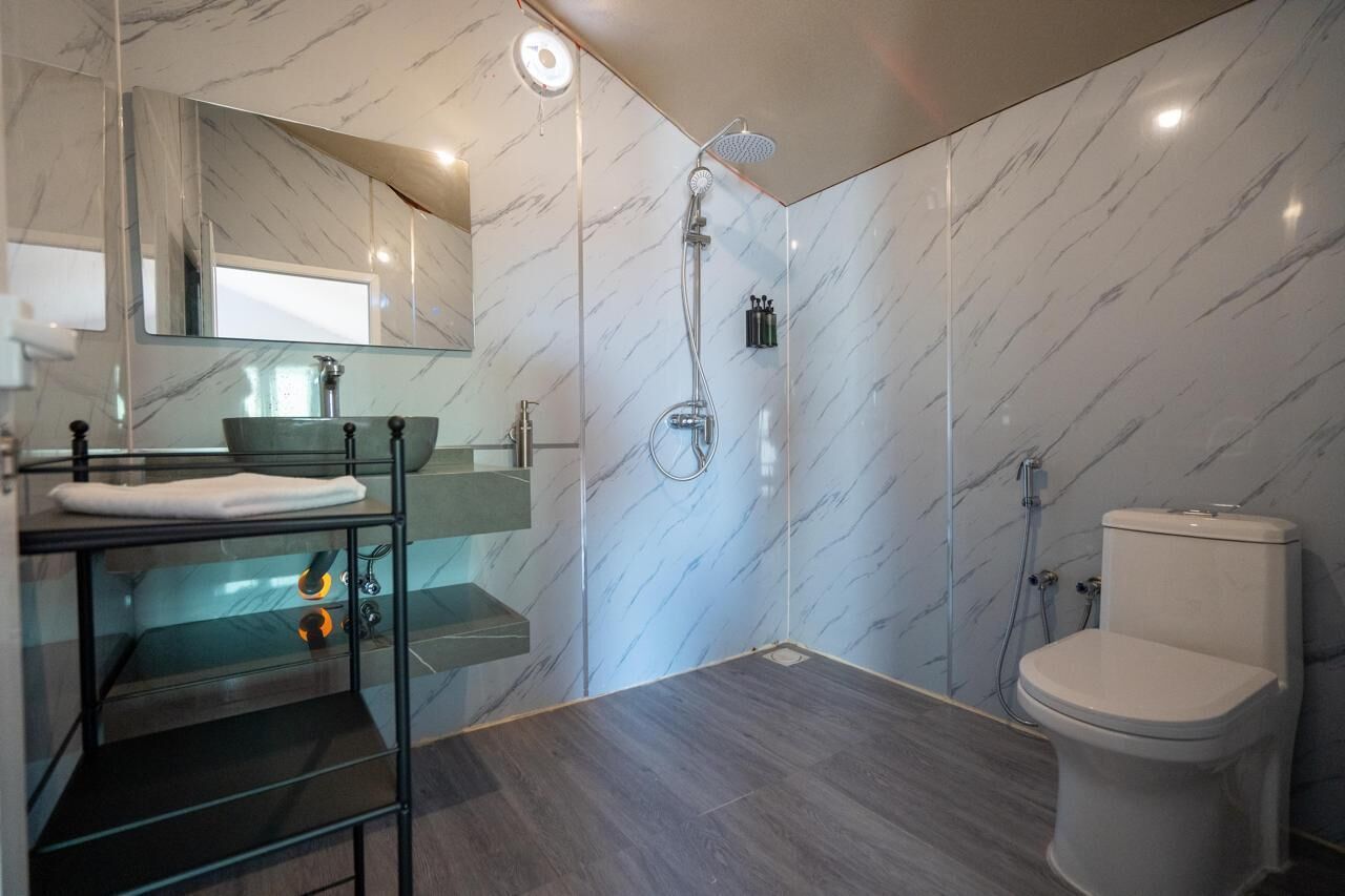 Een moderne badkamer met een marmeren wand, een glazen wastafel, een toilet en een douche.