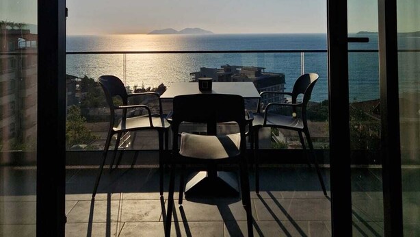 A balcony with a table and chairs overlooking a coastal view. - Vila Kendezi (Vlorë)